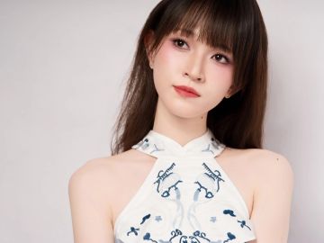 A woman with long hair wearing a white halter top with blue embroidery.