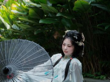A woman in traditional attire holding a parasol amidst lush greenery.