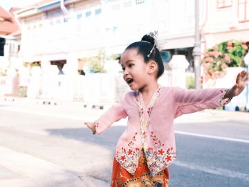 A joyful young girl standing in front of a gray door with greenery overhead.