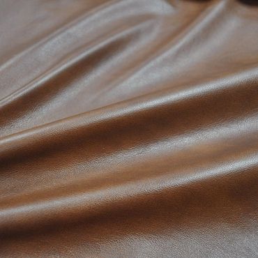 Close-up of smooth brown leather fabric with natural texture and gentle folds.