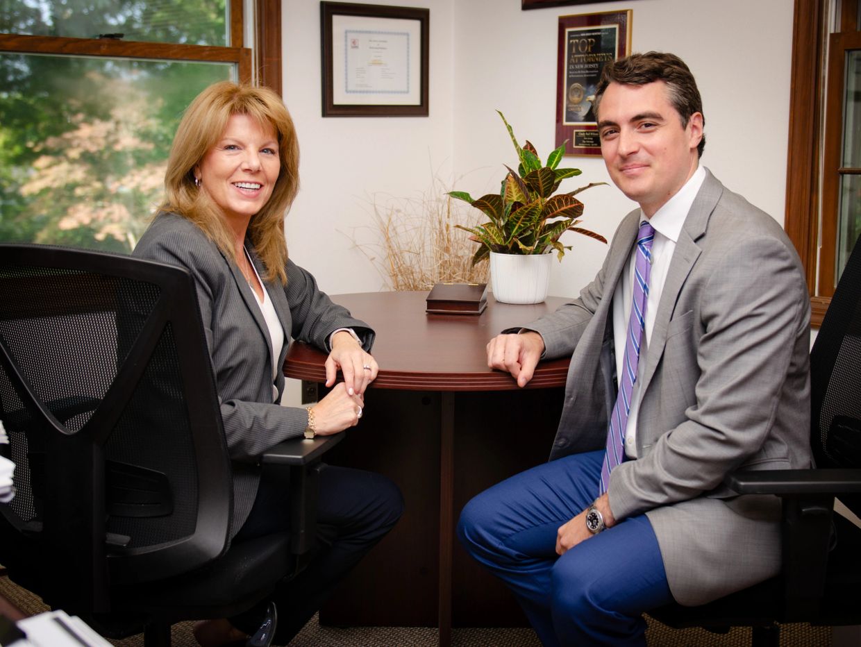 Two professionals in a meeting room, smiling at the camera.