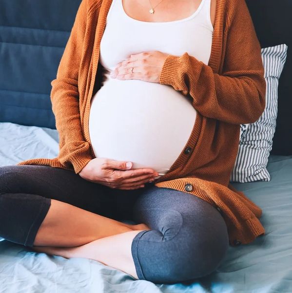 Pregnant women sitting on the bed holding her stomach