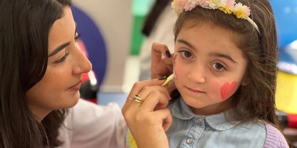 A woman painting a heart on a young girl's cheek.