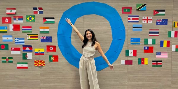 Young woman posing happily in front of international flags and a large blue circle on a wall.