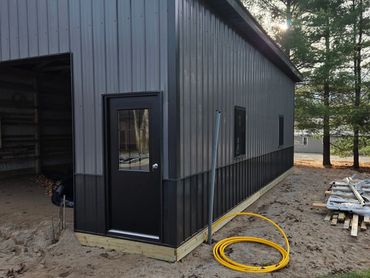 Metal building under construction with black door and yellow cable coil outside.