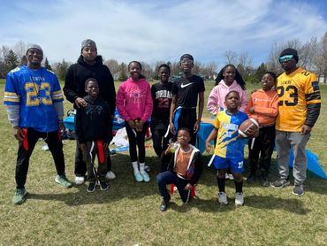 Group of kids and adults outdoors, some wearing sports jerseys and holding a football.