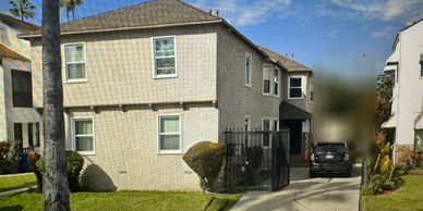 Two-story beige brick house with a driveway and a black car.