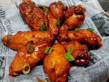 Glazed chicken wings with green onions on newspaper.