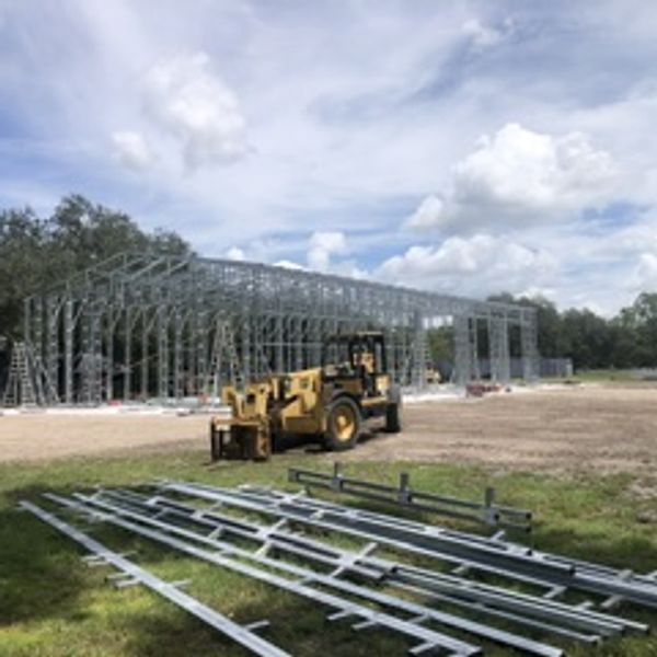 Construction site with steel framework and machinery under a cloudy sky.