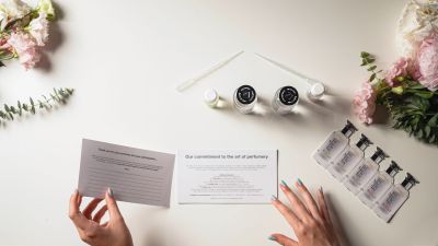 Hands reading a product information card next to perfume testing samples and flowers.