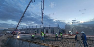 Construction workers pouring concrete on a building site at dusk.