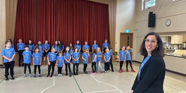 Group of children and a woman in a gymnasium, all wearing blue shirts.