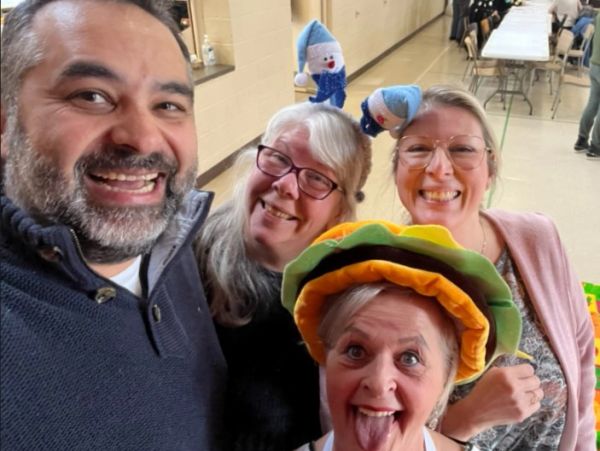 Four friends smiling indoors, one wearing fun headbands and a colorful hat.