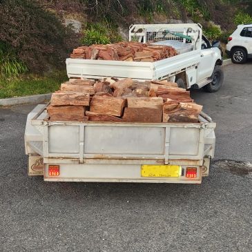 Two white pickup trucks loaded with chopped firewood on a paved road.