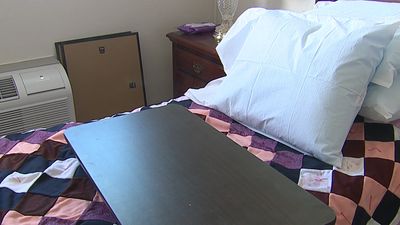 A bed with white pillows and a small black table on a colorful checkered blanket.