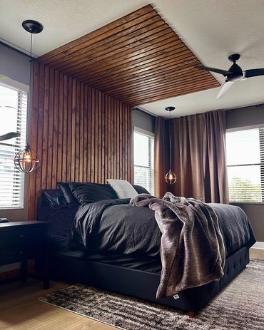 Modern bedroom with a wooden slat accent wall and ceiling, black bedding, and cozy lighting.