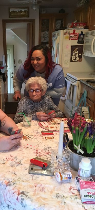 An elderly woman playing cards with a caregiver in a cozy kitchen setting.