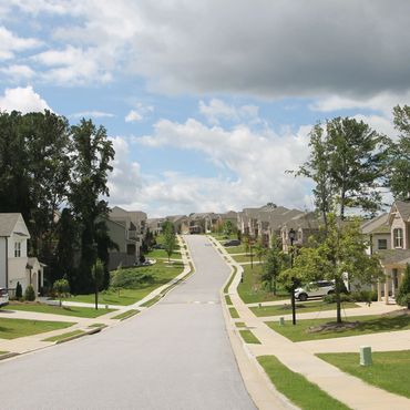 A quiet suburban street lined with modern houses and green lawns under a partly cloudy sky.