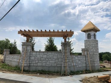 Stone wall and wooden pergola under construction with a tower on the side.