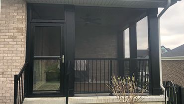 Screened porch with black metal frame and a small budding tree in front.