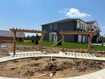 Two wooden pergolas on a curved sidewalk with houses in the background.
