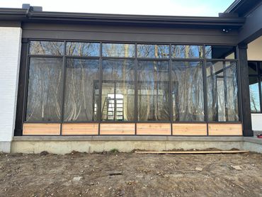 Large glass windows with wooden panels at the base on a modern house exterior.
