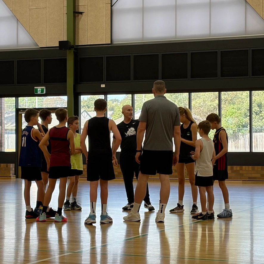 Coach instructing a group of young basketball players in a gym.