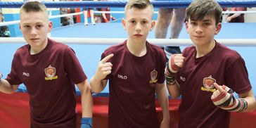 Three young boxers in maroon Galway Boxing Club shirts stand before a boxing ring.