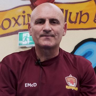 Man in maroon Galway Boxing Club shirt in front of boxing-themed mural.