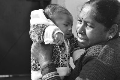 An elderly woman lovingly holds a baby wrapped in warm clothes.