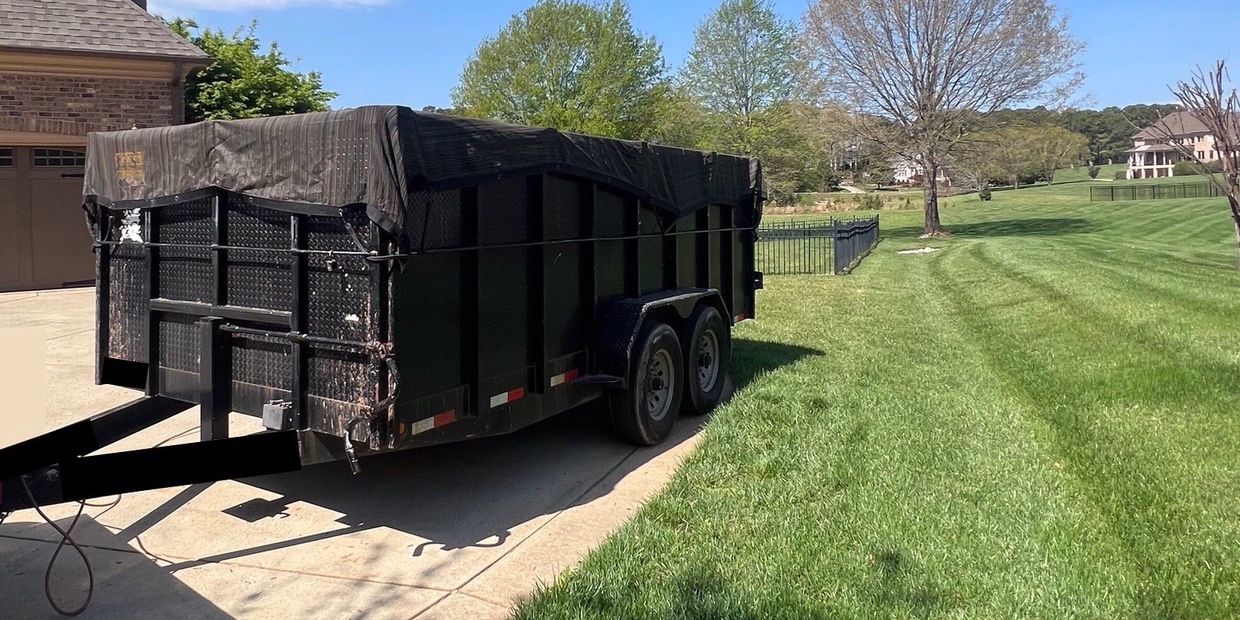 Black trailer parked on driveway beside green lawn.