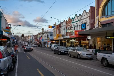 Busy street with shops and parked cars during dusk.