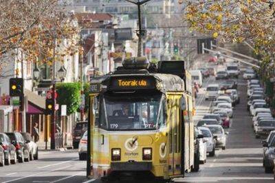 Yellow tram moving through a city street with traffic.