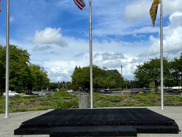 Empty black stage platform outdoors with flags and blue sky.