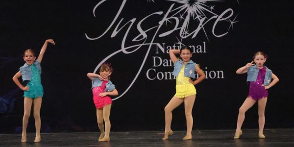 Four young dancers in colorful costumes pose on stage at a dance competition.