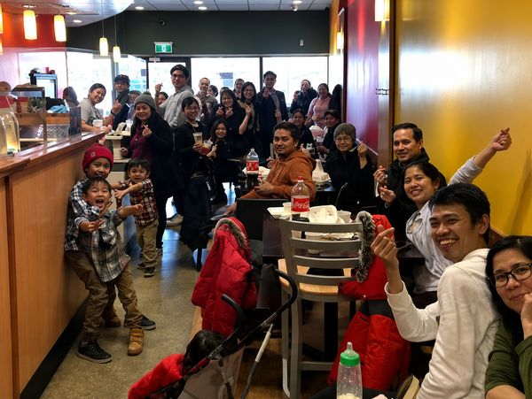 Group of people smiling and making finger heart gestures in a cozy restaurant.