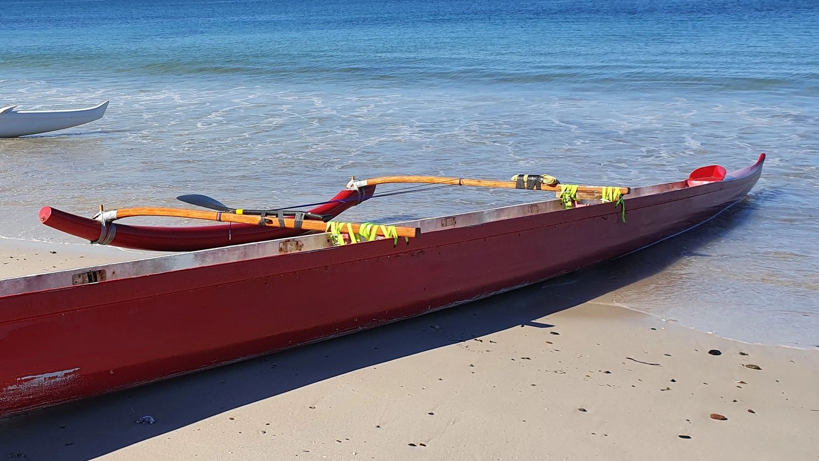 Red outrigger canoe on sandy beach with calm ocean.