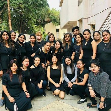 Group photo of young adults dressed mostly in black, outdoors near buildings and trees.