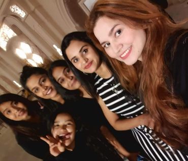 A group of six young women smiling and posing for a selfie indoors.