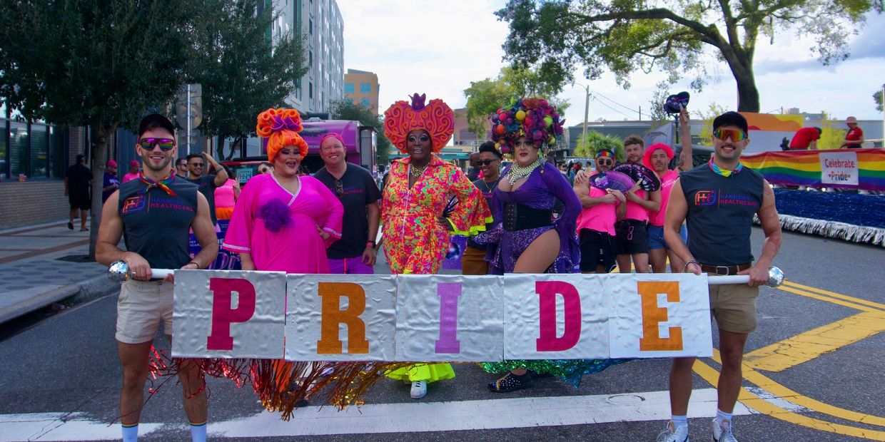 People celebrating pride holding colorful PRIDE sign at parade.