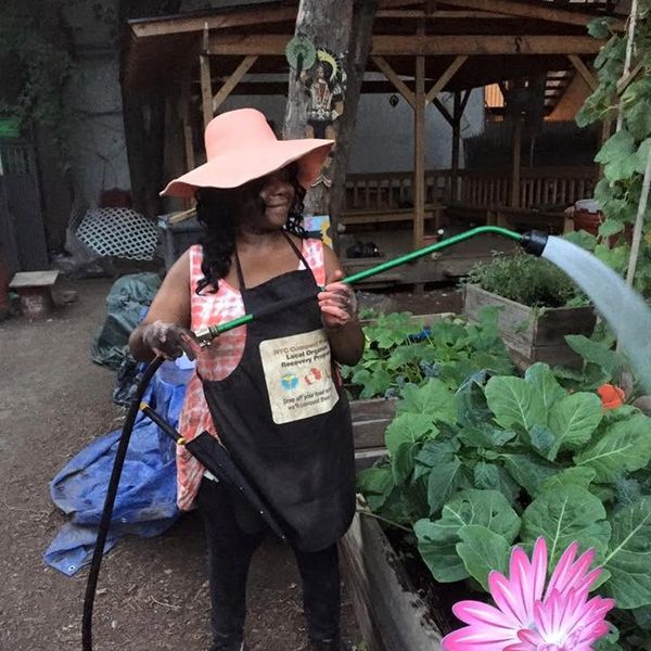 Woman watering plants in garden wearing a pink hat.