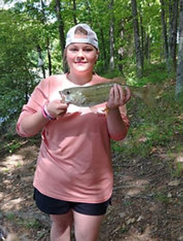 A person proudly holding a freshly caught fish in a wooded area.