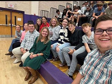 Group of smiling young people sitting on gym bleachers.