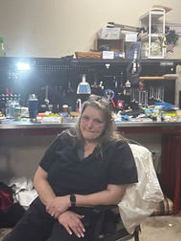 Woman sitting on a chair in a cluttered workshop or garage.