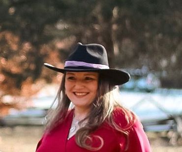Woman smiling outdoors wearing a black hat and red outfit.