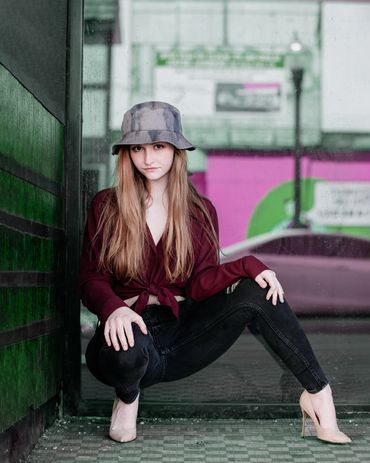 Girl posing wearing a hat, burgundy top, black pants and heels