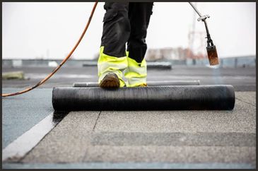 A roofer using a torch while rolling out the underlayment on a commercial roofing project