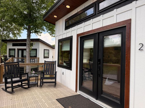 Two modern tiny houses with black framed doors and windows on a wooden deck.