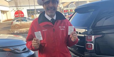 happy valet attendant in an alber-haff uniform holding two claim checks at the king of Prussia mall