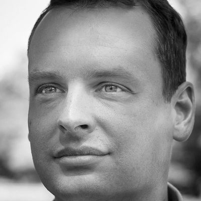 Close-up portrait of a man with green eyes and short dark hair outdoors.